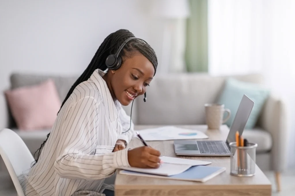 Mujer sentada sonriendo con diadema y laptop tomando notas de los cursos y clases de idiomas personalizadas